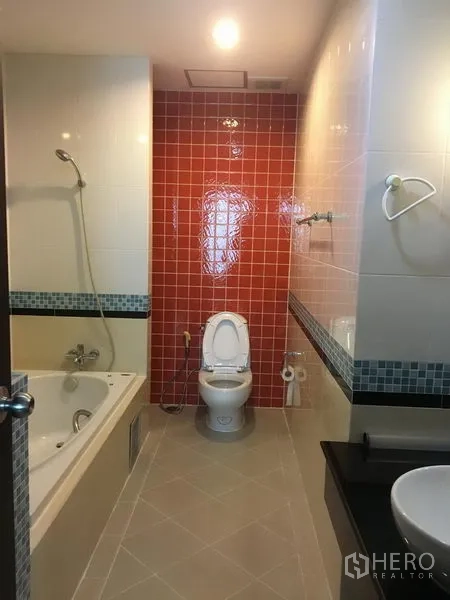 Condominium for rent in Khlong Toei, Bangkok - Second bathroom with red accent tiles, bathtub with shower, toilet and basin.