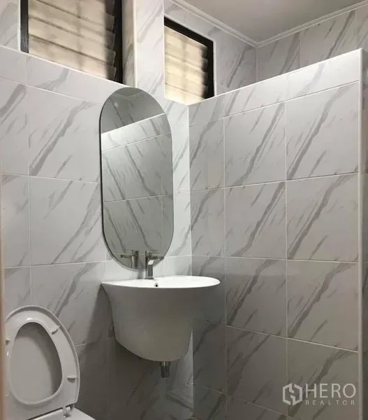 Detached House for rent in Khlong Toei, Bangkok - Compact bathroom with marble-look tiles, wall-mounted sink and oval mirror