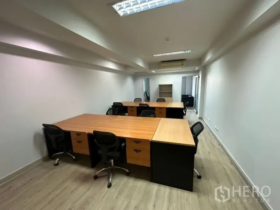 Office Space for rent in Khlong Toei, Bangkok - Open-plan office with multiple wooden workstations, black task chairs, wood-look flooring, white walls and ceiling fluorescent lights with wall-mounted air conditioning.