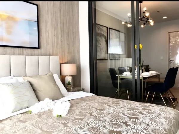Condominium for rent or sale in Pathum Wan, Bangkok - Cozy bedroom with upholstered headboard, patterned bedding and sliding glass doors opening to the dining area.