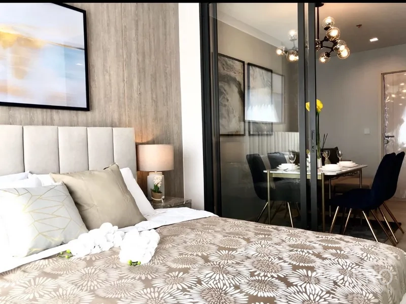 Condominium for rent or sale in Pathum Wan, Bangkok - Cozy bedroom with upholstered headboard, patterned bedding and sliding glass doors opening to the dining area.