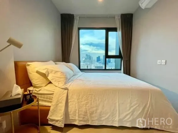 Condominium for rent in Pathum Wan, Bangkok - Cozy bedroom with large window showcasing a panoramic Bangkok skyline view.