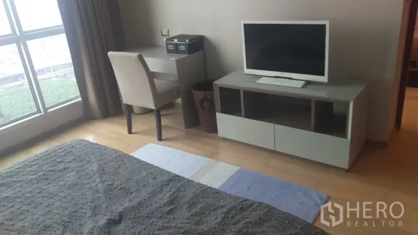 Condominium for rent in Ratchathewi, Bangkok - Bedroom corner with work desk, chair, TV console and large window over hardwood floors.
