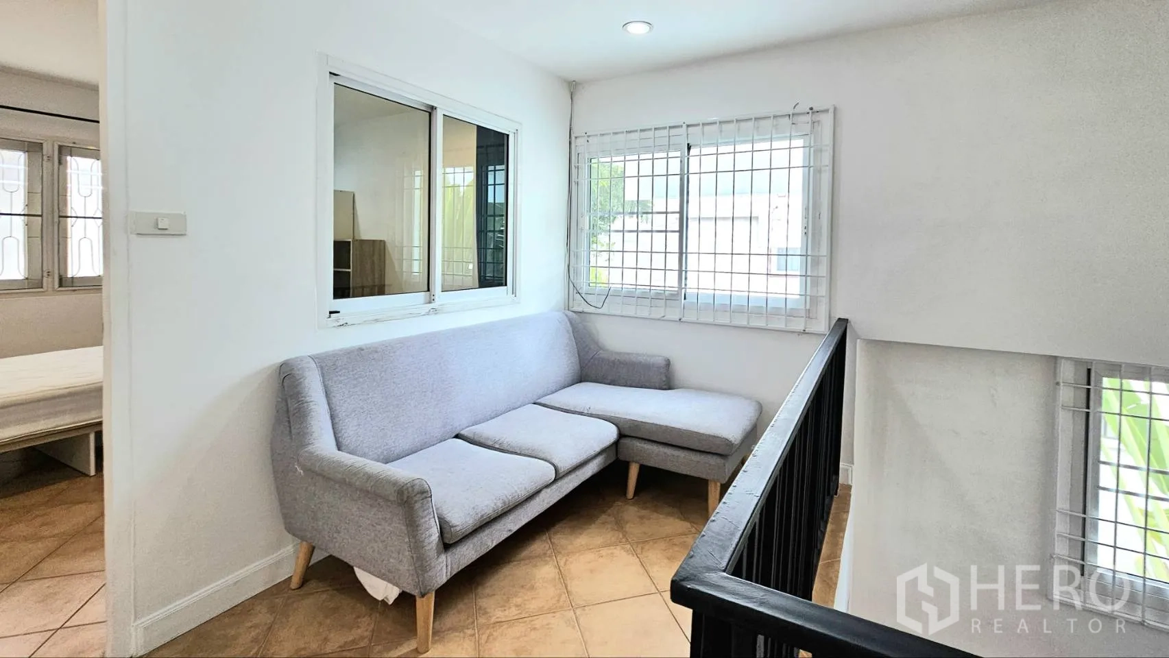 Detached House for rent in Saphan Sung, Bangkok - Upstairs landing lounge with gray L-shaped sofa beside windows with security grilles.