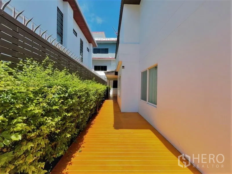 บ้าน ให้เช่าในSuan Luang, Bangkok - ทางเดินและชานไม้รับแสง แทรกด้วยรั้วบังสายตาและพุ่มไม้ตัดแต่ง.