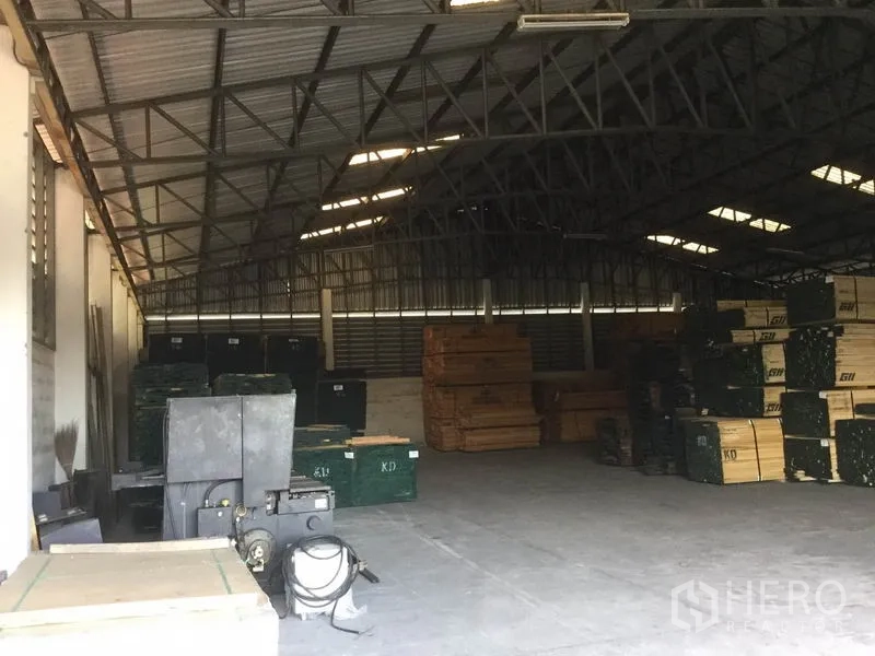 Warehouse for sale in Sai Noi, Nonthaburi - Warehouse interior with steel truss roof, concrete floor, and stacked pallets.