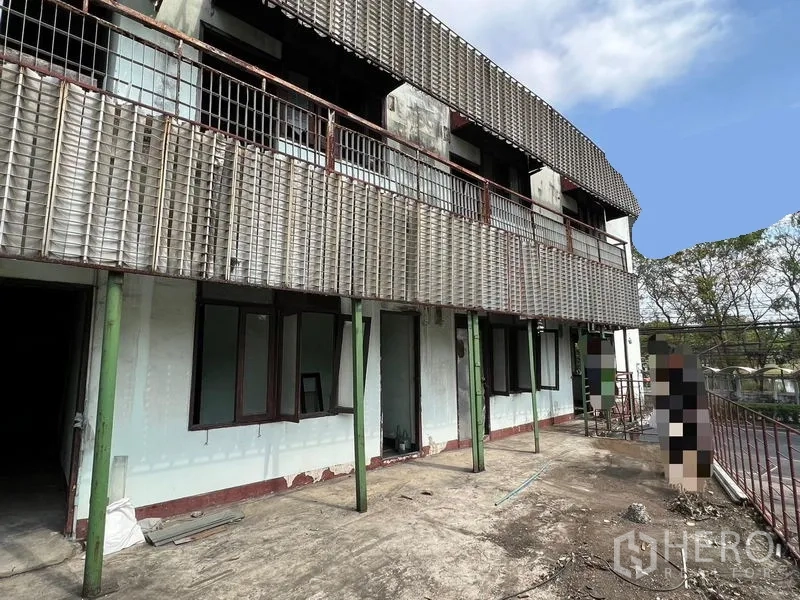 Shophouse for rent or sale in Bang Khen, Bangkok - Rear terrace with long metal-grille balcony and concrete walkway outside the units.
