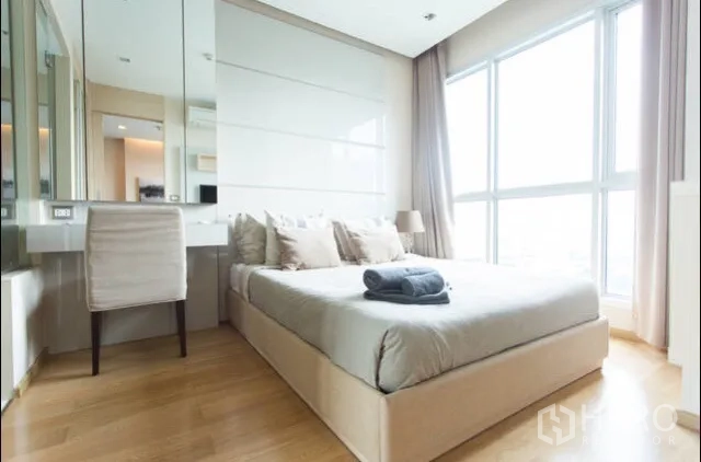 Condominium for rent in Ratchathewi, Bangkok - Sunlit bedroom with floor-to-ceiling windows, neutral decor and built-in vanity desk.