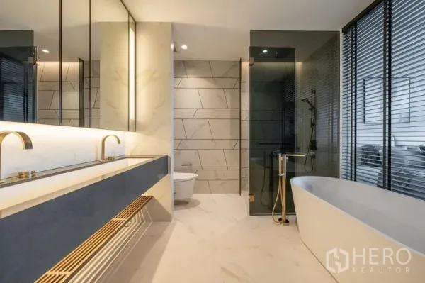 公寓 出租在Khlong Toei, Bangkok - 现代卫浴，双台盆、独立浴缸与玻璃淋浴间，金色龙头点缀。