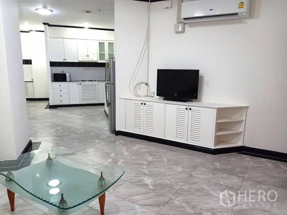 คอนโด for rent in Watthana, Bangkok - มุมห้องนั่งเล่นพร้อมชั้นวางทีวีและโต๊ะกลางกระจก มองไปยังครัวกว้าง