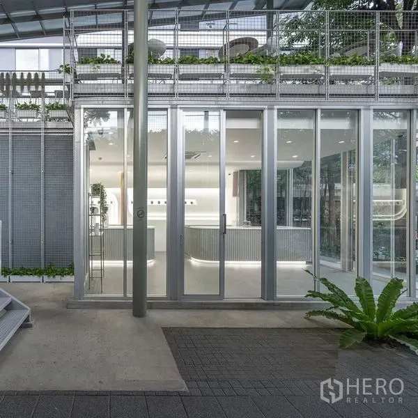พื้นที่ขายปลีก ให้เช่าในKhlong Toei, Bangkok - ด้านหน้าอาคารชั้นล่างกับประตูกระจกเลื่อน โครงโลหะ และต้นไม้เขียวขจีของพื้นที่ค้าปลีกทันสมัย