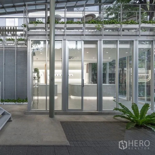 พื้นที่ขายปลีก ให้เช่าในKhlong Toei, Bangkok - ด้านหน้าอาคารชั้นล่างกับประตูกระจกเลื่อน โครงโลหะ และต้นไม้เขียวขจีของพื้นที่ค้าปลีกทันสมัย