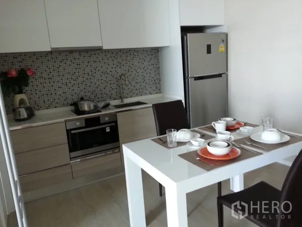 Condominium for rent in Watthana, Bangkok - Compact kitchen with mosaic backsplash, built-in oven, stainless fridge and a dining table for two.