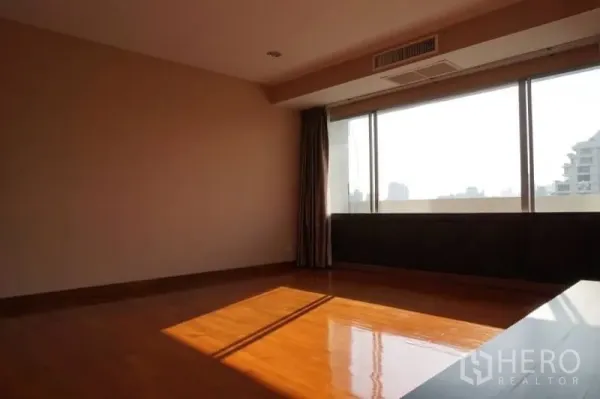 Condominium for rent in Watthana, Bangkok - Sunlit empty room with wide windows, city outlook and polished parquet flooring.