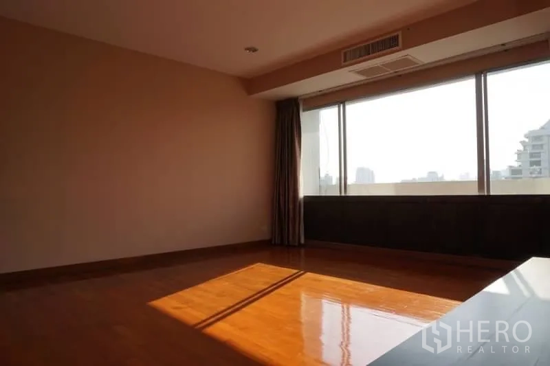 Condominium for rent in Watthana, Bangkok - Sunlit empty room with wide windows, city outlook and polished parquet flooring.