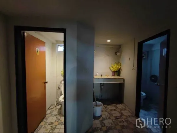 Shophouse for rent in Khlong Toei, Bangkok - Restroom area with two doors and a shared sink on patterned tile flooring.