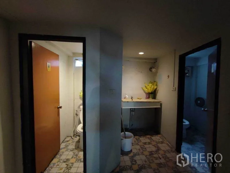 Shophouse for rent in Khlong Toei, Bangkok - Restroom area with two doors and a shared sink on patterned tile flooring.