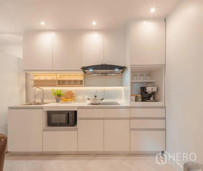 Condominium for sale in Yan Nawa, Bangkok - Straight-on white kitchen with cooktop, hood, sink, microwave, and coffee nook.