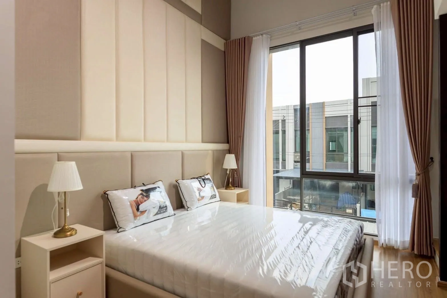 Townhouse for rent or sale in Bang Phli, Samut Prakan - Sunlit bedroom corner with tall window, drapes and a bedside table with lamp.