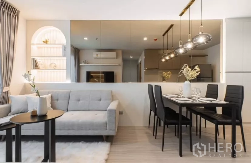 Condominium for rent in Chatuchak, Bangkok - Cozy lounge with grey sofa, arched built‑in shelves and a dining set beside a large mirror.