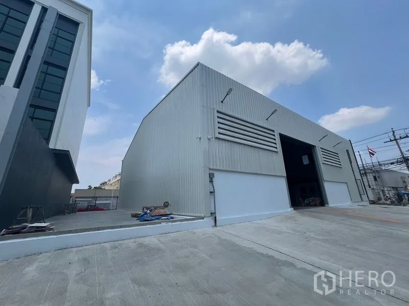 货栈 出租在Bang Sao Thong, Samut Prakan - 金属板外墙侧立面，大型卷帘门与宽阔车道装卸区。