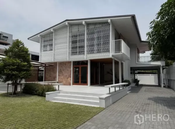 Detached House for rent in Watthana, Bangkok - Front exterior of a renovated mid-century detached house with patterned facade, lawn and paved driveway.