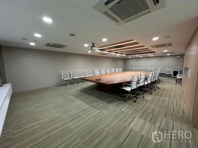 Office Space for rent - Large boardroom featuring a central wooden table, white swivel chairs, projector and recessed lighting.