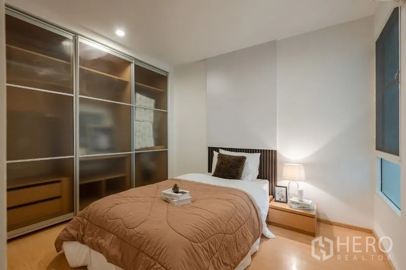 Condominium for sale in Watthana, Bangkok - Second bedroom with sliding-door wardrobes, bedside lamp and window.