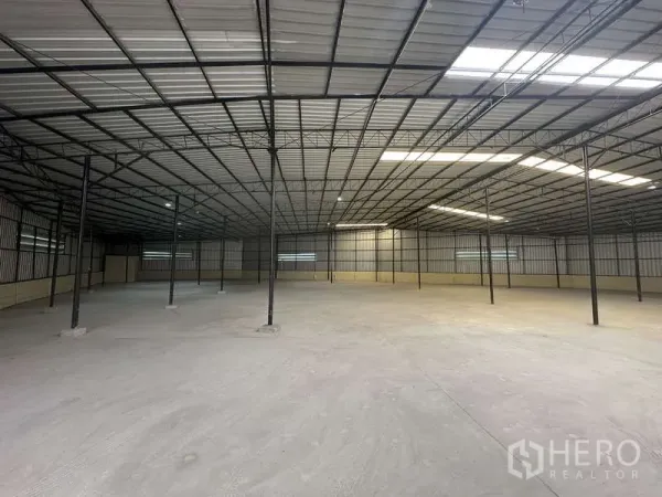 Warehouse for rent in Pak Kret, Nonthaburi - Spacious open-plan warehouse interior with steel truss roof, skylights, and concrete floor.