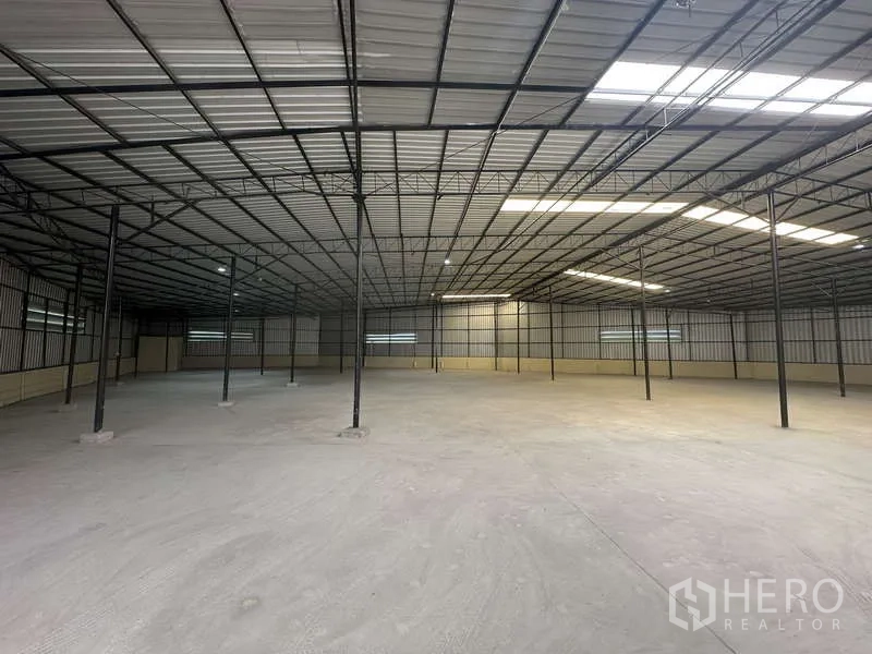 Warehouse for rent in Pak Kret, Nonthaburi - Spacious open-plan warehouse interior with steel truss roof, skylights, and concrete floor.