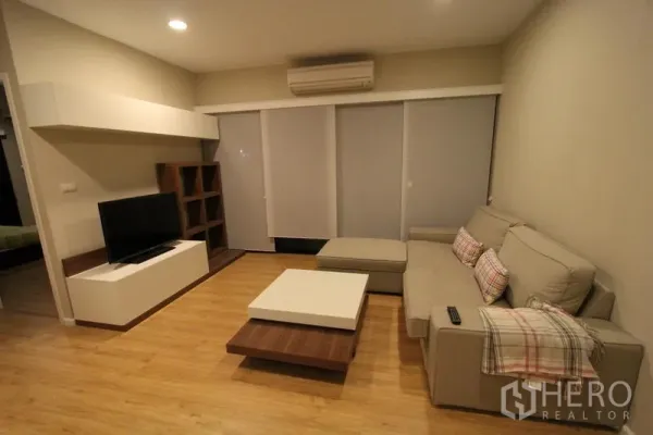 คอนโด ให้เช่าในPathum Wan, Bangkok - ห้องนั่งเล่นสบายๆ โซฟาเข้ามุม ชั้นวางทีวี พื้นไม้ และประตูกระจกบานเลื่อนพร้อมม่าน