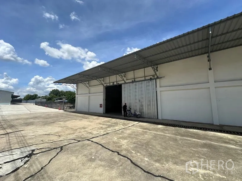 货栈 出租在Mueang Pathum Thani, Pathum Thani - 仓库斜角外观，宽阔车道、带顶装卸区与超大滑动入口。