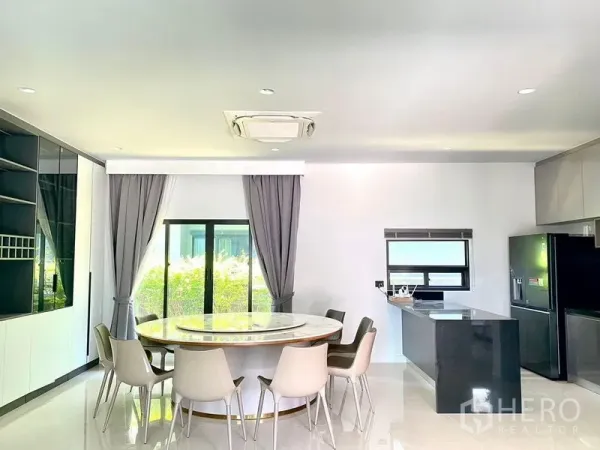Detached House for sale in Bang Kapi, Bangkok - Bright dining area with a round table, grey curtains and garden view next to the kitchen.