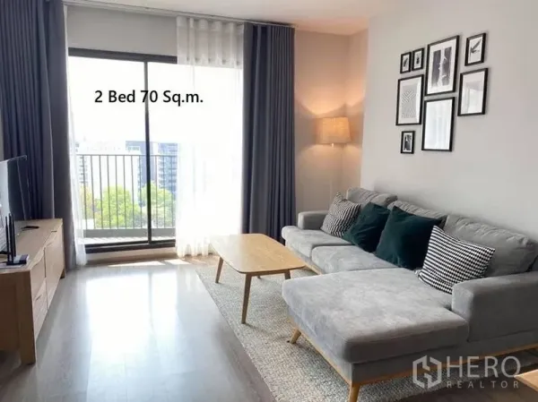 Condominium for rent in Watthana, Bangkok - Cozy lounge with sectional sofa, TV console and sliding door to a small balcony with city view.