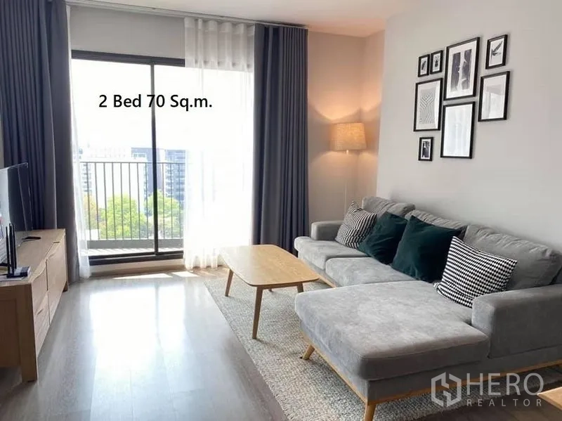 Condominium for rent in Watthana, Bangkok - Cozy lounge with sectional sofa, TV console and sliding door to a small balcony with city view.