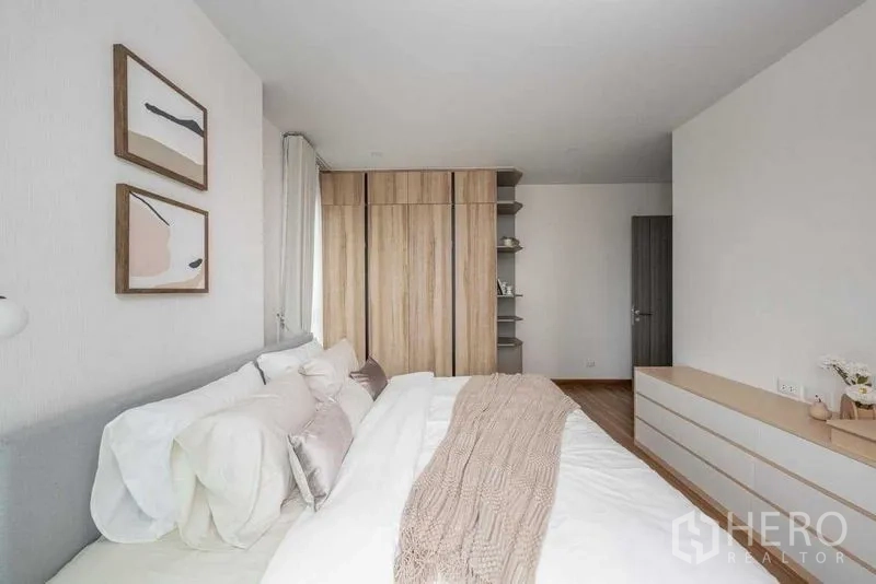 คอนโด ให้เช่าในKhlong San, Bangkok - ห้องนอนหลัก เตียงคิงส์ ตู้เสื้อผ้าไม้ ชั้นวางของ และภาพตกแต่งสไตล์มินิมอล