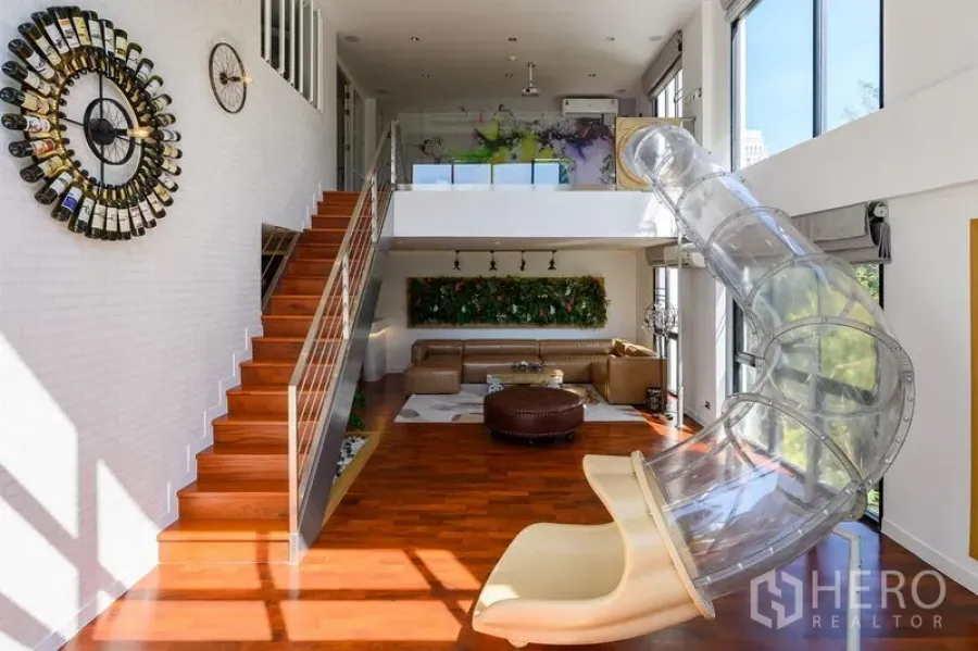 Condominium for rent in Pathum Wan, Bangkok - Mezzanine living area with staircase, wine-bottle wall clock, and clear indoor slide.