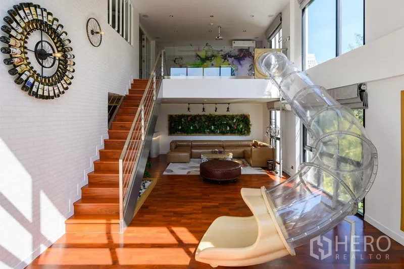 Condominium for rent in Pathum Wan, Bangkok - Mezzanine living area with staircase, wine-bottle wall clock, and clear indoor slide.