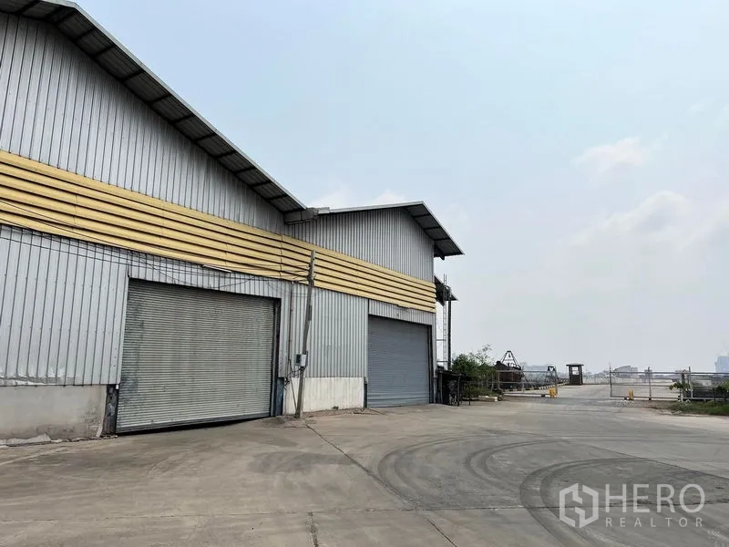 Warehouse for rent in Phra Samut Chedi, Samut Prakan - Warehouse exterior with big roller shutters next to the riverfront.