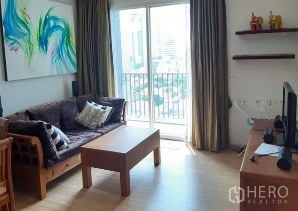 คอนโด ให้เช่าในKhlong Toei, Bangkok - ห้องนั่งเล่นสว่าง โซฟาไม้ โต๊ะกลาง และประตูกระจกสไลด์ออกสู่ระเบียงวิวเมือง