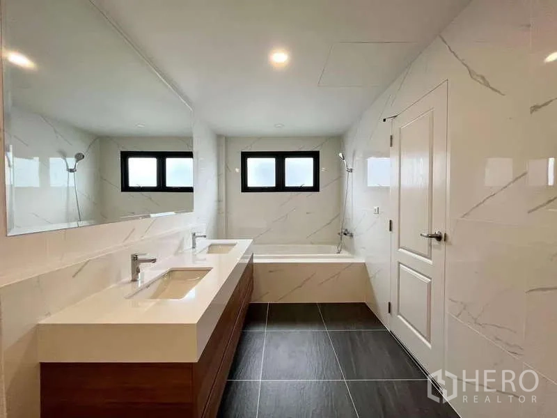 Detached House for rent in Don Mueang, Bangkok - Bright bathroom featuring double vanity, bathtub and marble-look walls.