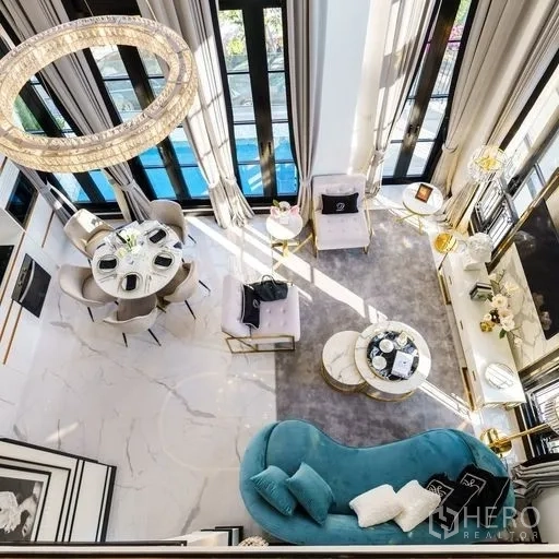 Townhouse for sale - Double-height living and dining area with marble floors, crystal chandelier, tall windows, teal sofa and round dining table.