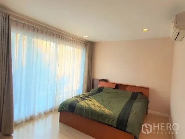 Townhouse for rent in Wang Thonglang, Bangkok - Bedroom with floor-to-ceiling sheer curtains opening to a balcony.