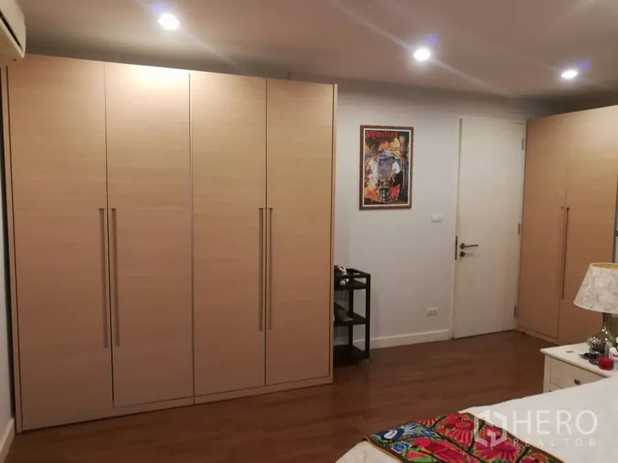 Condominium for rent in Watthana, Bangkok - Bedroom with full-height wood wardrobes, recessed lighting and warm wooden floors.