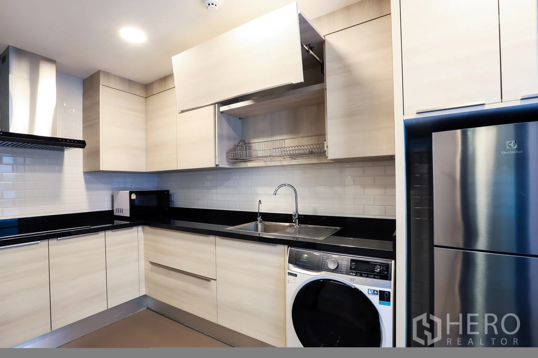 Condominium for rent in Watthana, Bangkok - Modern L-shaped kitchen with light cabinets, black countertops, subway tile backsplash and an in-unit washer.