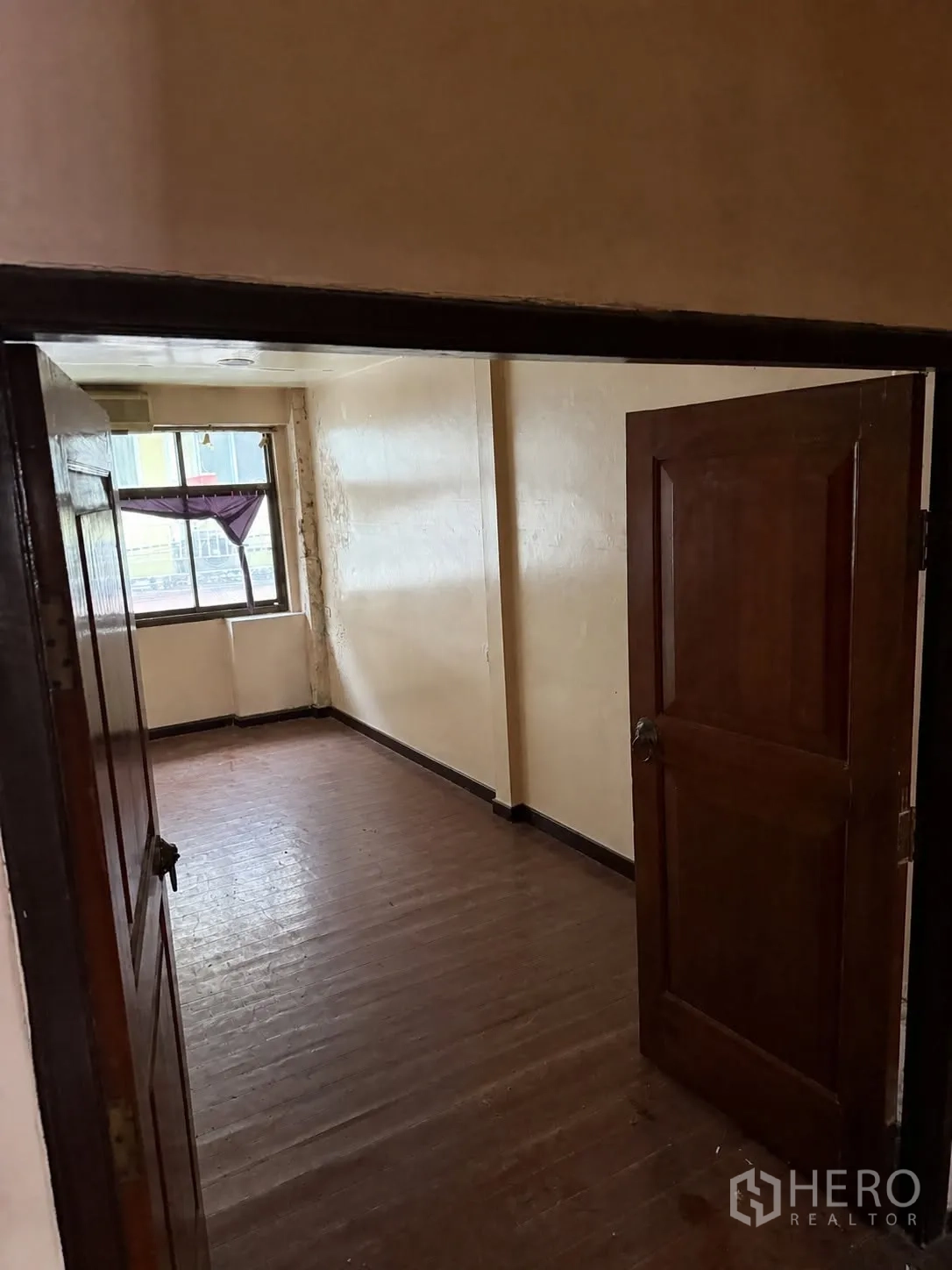 Shophouse for rent in Bang Rak, Bangkok - Compact room with wooden floor, cream walls and a window seen through an open wooden door.