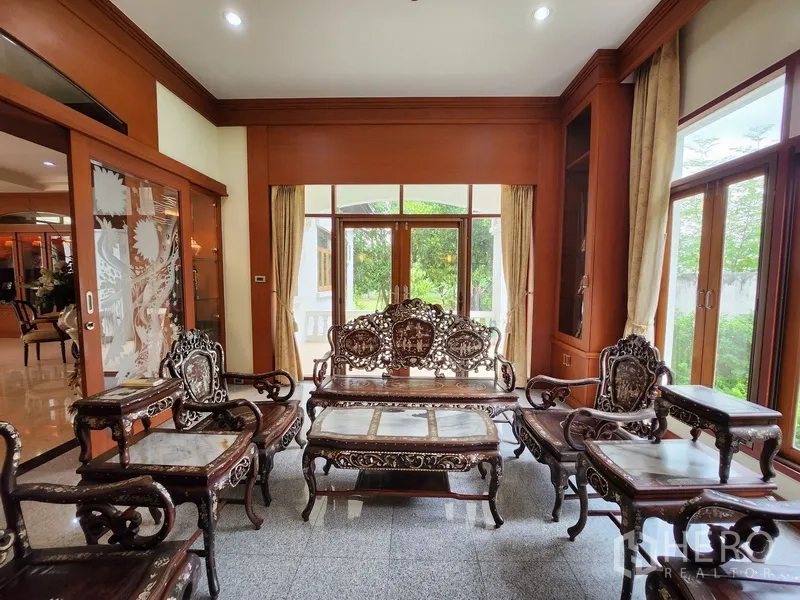 独立式住宅 出租在Prawet, Bangkok - 雅致会客室，雕花木质家具，玻璃门外连通花园景观。