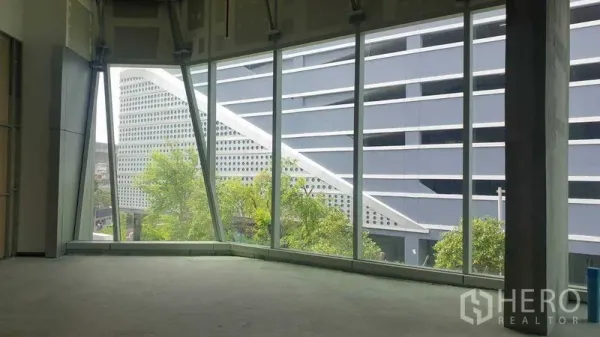 零售空间 出租 - 未装修零售铺面，落地窗俯瞰现代建筑与绿树景观。
