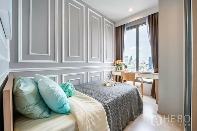 Condominium for rent or sale in Watthana, Bangkok - Cozy bedroom with large window, study desk and skyline outlook.