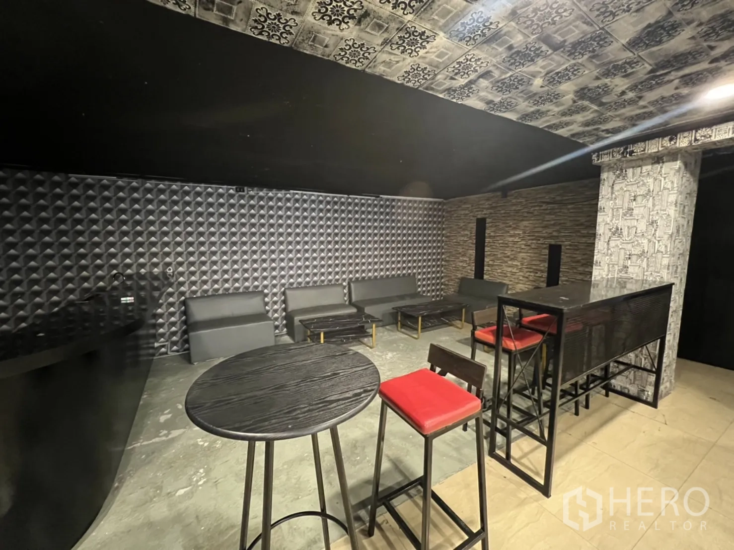 零售空间 出租在Watthana, Bangkok - 现代沙发角落，配高桌与红色吧凳，几何墙板背景。